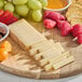 A wooden cutting board with a block of Entremont Comte cheese, fruit, and crackers.