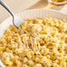 Shredded Ammerlander Smoked Gouda cheese on a fork over a bowl of macaroni and cheese.