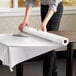 A person rolling a Choice white plastic table cover roll onto a table.
