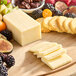 A wooden cutting board with a block of Ammerlander Gouda cheese, fruit, and crackers.