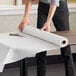 A hand cutting a roll of Choice white paper table cover on a table.