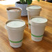 World Centric compostable bamboo hot cup lids on three white cups of coffee on a wooden table.