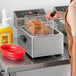 A woman using a Main Street Equipment electric countertop fryer to cook fried chicken.