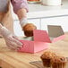 A person holding a muffin and putting it into a pink Southern Champion bakery box.