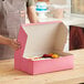 A woman holding a Southern Champion pink cake box with flowers inside.