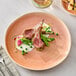An Acopa Highlands Primrose Peach coupe china plate with meat and vegetables on it.