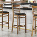 A Lancaster Table & Seating wood ladder back bar stool with a black vinyl seat cushion detached.