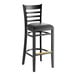 A Lancaster Table & Seating black wood ladder back bar stool with black vinyl seat on a table in a bar.