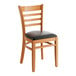 A Lancaster Table & Seating wooden ladder back chair with a black vinyl seat on a wooden surface.