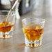 A person pouring brown liquid into two Acopa Memphis glasses on a table.