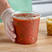 A hand holding a Choice plastic deli container of tomato sauce.