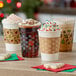 Choice snowflake printed coffee cup sleeves on three coffee cups with whipped cream and sprinkles on a table.