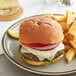 A cheeseburger with tomato and onion on a King's Hawaiian sandwich roll on a plate.