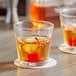 Two Acopa Memphis rocks glasses with whiskey and cherries on a table.