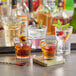 A group of Acopa Memphis rocks glasses with different colored drinks on a bar counter.