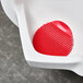 A red rubber urinal screen with a red plastic pad with a cherry design.