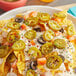 A bowl of nachos with jalapenos and white sauce.