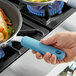 A hand using a blue Vigor silicone handle sleeve to hold a pan of food.
