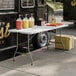 A Lancaster Table & Seating granite white plastic folding table set up with food containers and bottles of liquid.