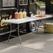 A white Lancaster Table & Seating bi-folding table with food items on it.