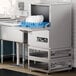 A Noble Warewashing undercounter dishwasher on a metal stand with plates in it.