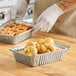 A gloved hand preparing food in a Western Plastics oblong foil take-out container.