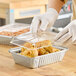 A person in gloves putting food in a Western Plastics oblong aluminum foil container.