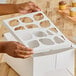 A person holding a white box with a Southern Champion cupcake insert with cut out holes for 12 cupcakes.