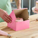 A person opening a pink Southern Champion cake box with a cake inside.