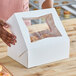 A person holding a white box with a clear plastic window containing donuts.