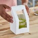 A person holding a Southern Champion white bakery box with a green cupcake inside.