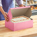 A person opening a Southern Champion pink cake box to reveal a cake with white and orange frosting.