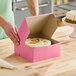 A person cutting a cake with white frosting in a Southern Champion pink bakery box.