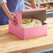 A woman opening a Southern Champion pink cake box to reveal a cake inside.