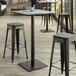 A Lancaster Table & Seating Excalibur bar height table with a textured Toscano finish and square base plate with stools on a patio.