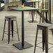 A Lancaster Table & Seating bar height table with a textured metal finish and square base plate with stools on a patio.