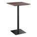 A Lancaster Table & Seating Excalibur bar height table with a textured walnut square top and a black square base.