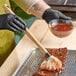 A person in black gloves using a Backyard Pro BBQ brush mop to baste ribs on a grill.