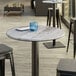 A Lancaster Table & Seating Excalibur round table with a blue glass on it and textured wood surface.