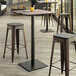 A Lancaster Table & Seating bar height table with textured mixed plank finish and a square base plate with stools on an outdoor patio.
