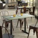 A Lancaster Table & Seating rectangular table with a textured metal finish on an outdoor patio with chairs and yellow cups.