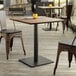 A Lancaster Table & Seating Excalibur square table with a textured farmhouse finish on a wood floor with two brown chairs