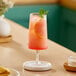 An Acopa Lore goblet filled with a pink drink with a slice of lemon and mint on a white table.