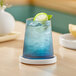 A blue stemless wine glass with a drink, ice, and a lime slice on a table.