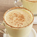 A glass mug of white liquid with brown sprinkles on top.