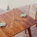 A Lancaster Table & Seating Tigerwood outdoor table set with plates, silverware, and a green napkin under a white umbrella.