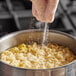 A gloved hand pouring Badia MSG powder into a bowl of noodles.