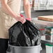 A woman holding a Lavex black drawstring trash bag.