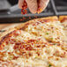 A person's hand sprinkling Badia Crushed Red Pepper on a pizza.