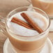 A glass mug of hot coffee with cinnamon sticks on the side.